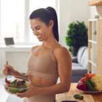 Slender fitness woman in sportswear standing at home in the kitchen with a bowl of fresh salad