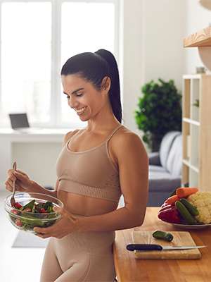 Slender fitness woman in sportswear standing at home in the kitchen with a bowl of fresh salad